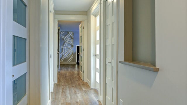 Beautiful long hallway filled with white doors accented with glass panels leading to master bedroom.